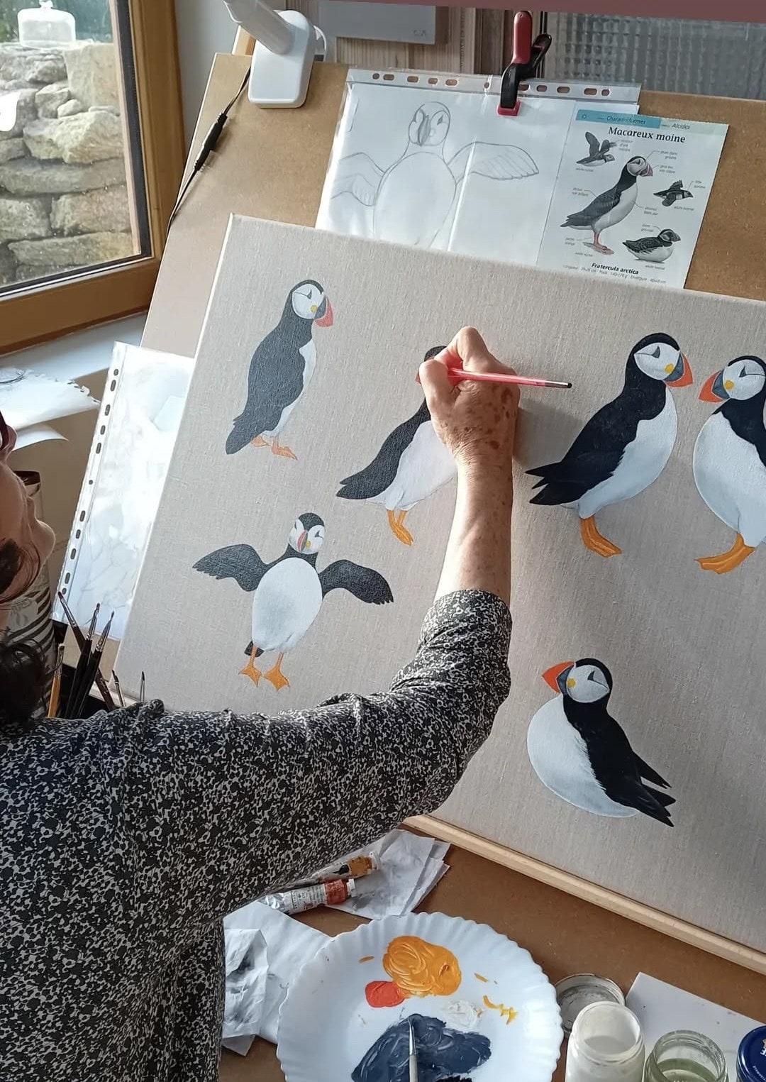 Carine Marchand en train de peindre des macareux dans son atelier