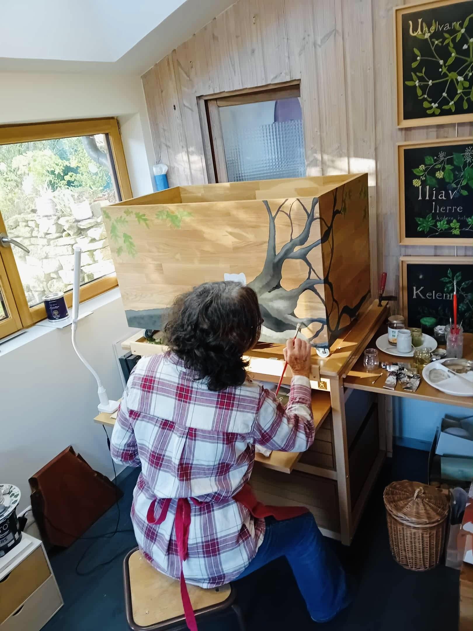 Carine peignant un meuble en bois dans son atelier